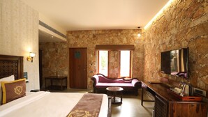 A hotel room with a bed, a sofa, a television, and a stone wall. - Vikrama Heritage Resort Pavagadh (Halol)
