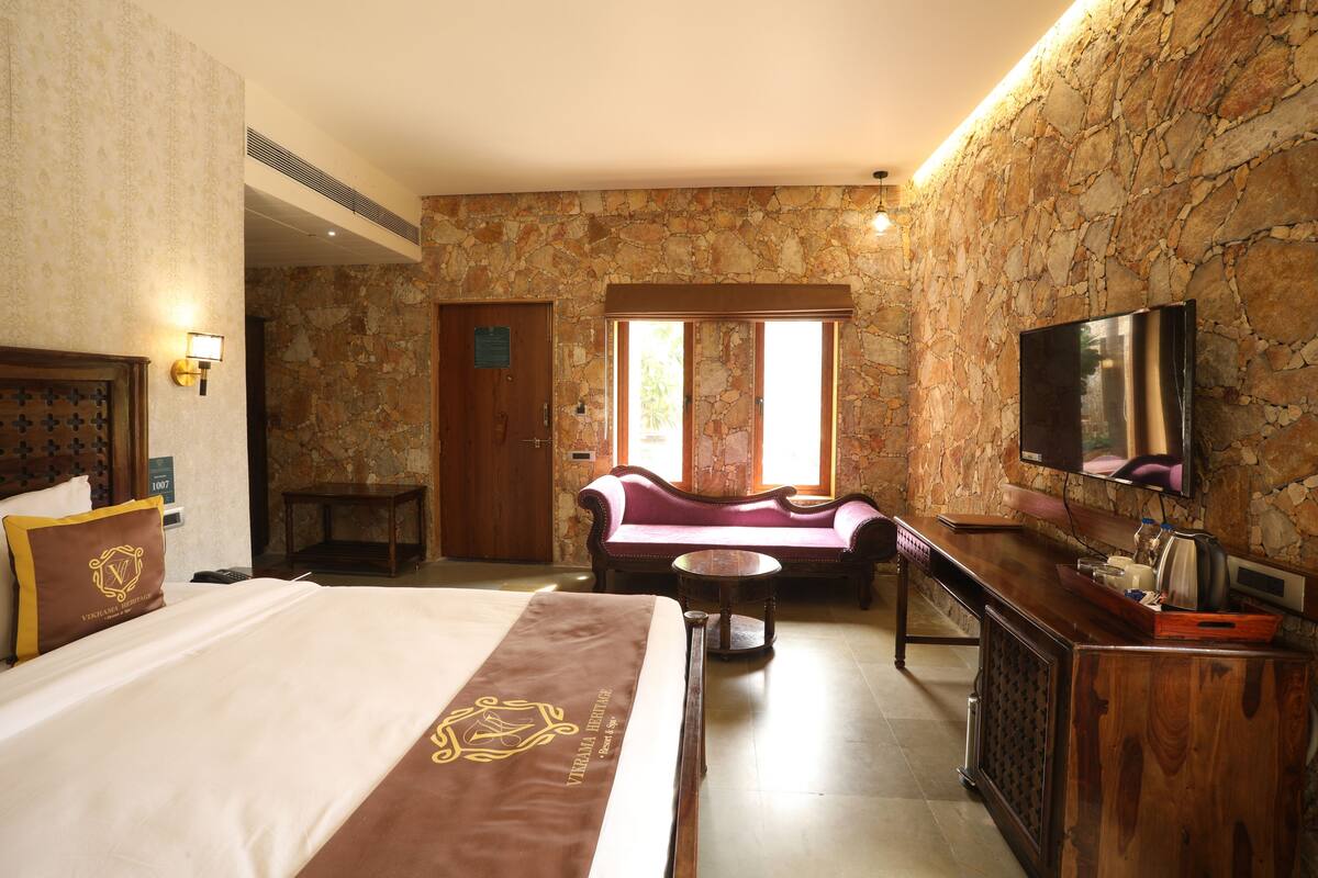 Une chambre d’hôtel avec un lit, un canapé, une télévision et un mur en pierre.