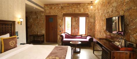 A hotel room with a bed, a sofa, a television, and a stone wall.