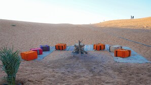 A desert campsite with several orange bags arranged on a blue mat, a small plant, and a rope leading up a hill.
