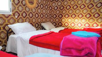 Quarto com papel de parede estampado, cama com roupa de cama branca e vermelha, e uma janela.