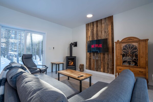 Una sala de estar moderna con un sofá, una mesa de centro de madera, una chimenea y un televisor montado en una pared de madera.