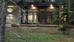 Eine moderne Hütte mit großen Fenstern, einer Veranda und Blick auf den umliegenden Wald.