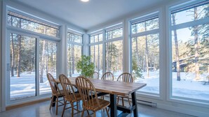 Ein Esszimmer mit großem Tisch und Stühlen, großen Fenstern und Blick auf einen verschneiten Wald.