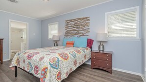 Une chambre à coucher comprenant un lit, deux tables de chevet, un élément décoratif fixé au mur et une porte donnant sur une autre pièce.