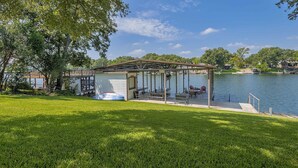 Un belvédère au bord du lac, doté de tables et de chaises pour pique-nique, entouré d’une pelouse et d’arbres.