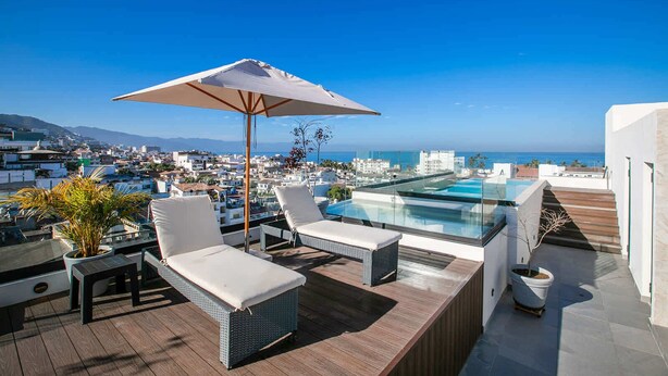 A rooftop terrace with a glass infinity pool, white lounge chairs, and a large umbrella. - Torre Doze Private Penthouse (Puerto Vallarta)
