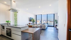 A modern kitchen with a central island, built-in oven, and a large window overlooking the city. - Torre Doze Private Penthouse (Puerto Vallarta)