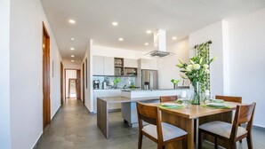 A modern kitchen with white cabinets, a central island, and a dining area with a wooden table and chairs. - Torre Doze Private Penthouse (Puerto Vallarta)