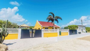 Un bâtiment jaune avec un toit rouge, entouré d’une clôture blanche et d’un palmier.
