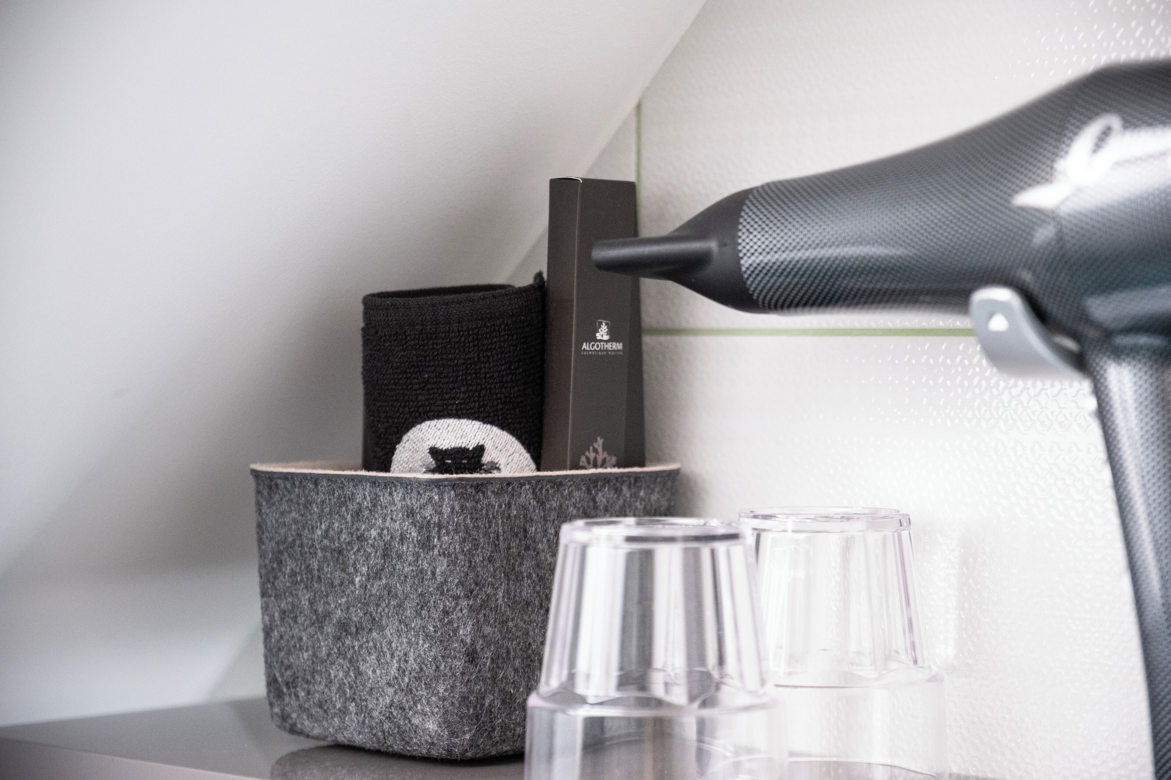 Un coin de pièce avec une boîte noire portant l’inscription « ALGOTHERM », un récipient gris texturé contenant un objet noir, et une bouteille en verre transparent.