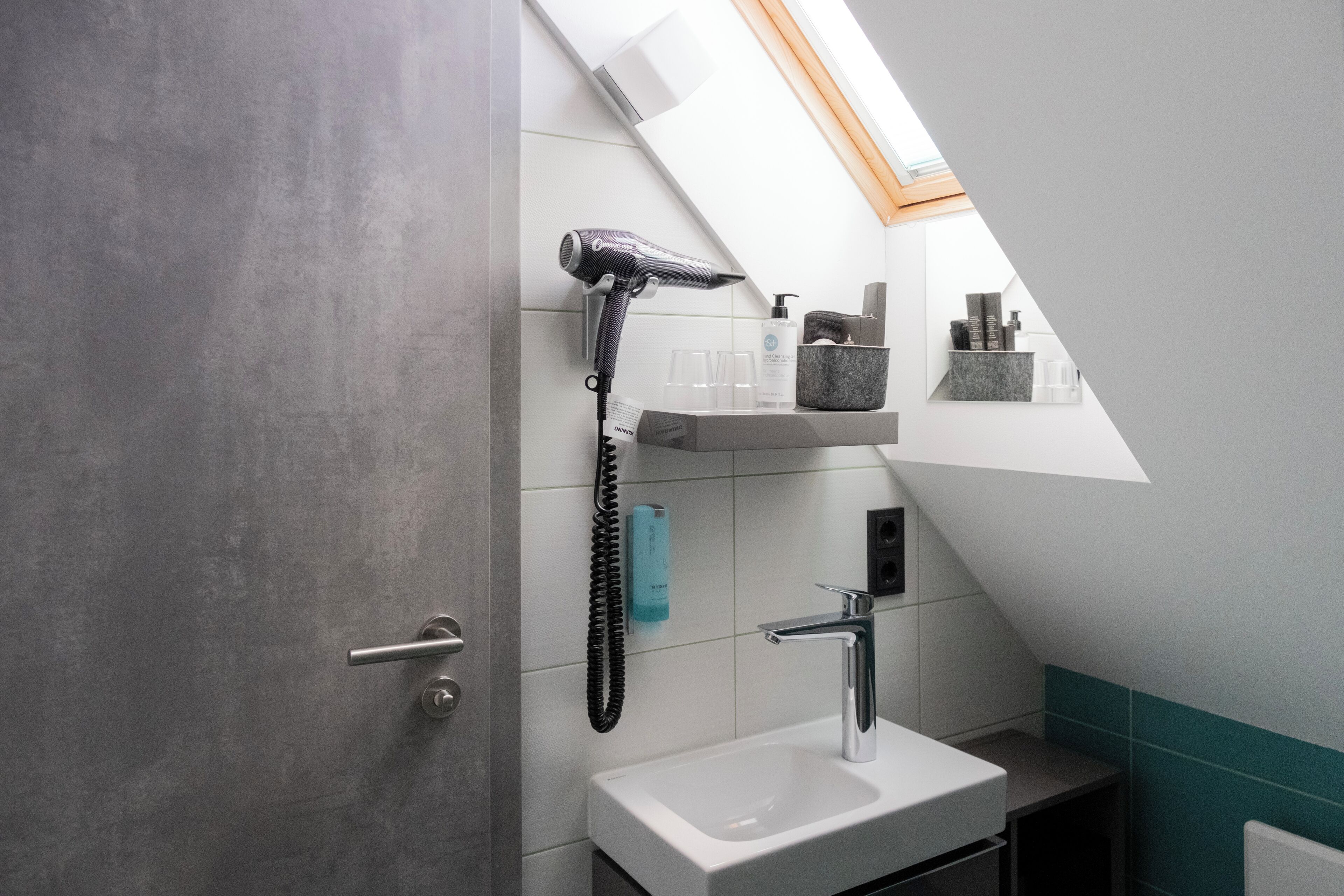 Une salle de bain moderne dotée d’une lucarne, d’un sèche-cheveux, d’un lavabo et d’étagères de rangement.