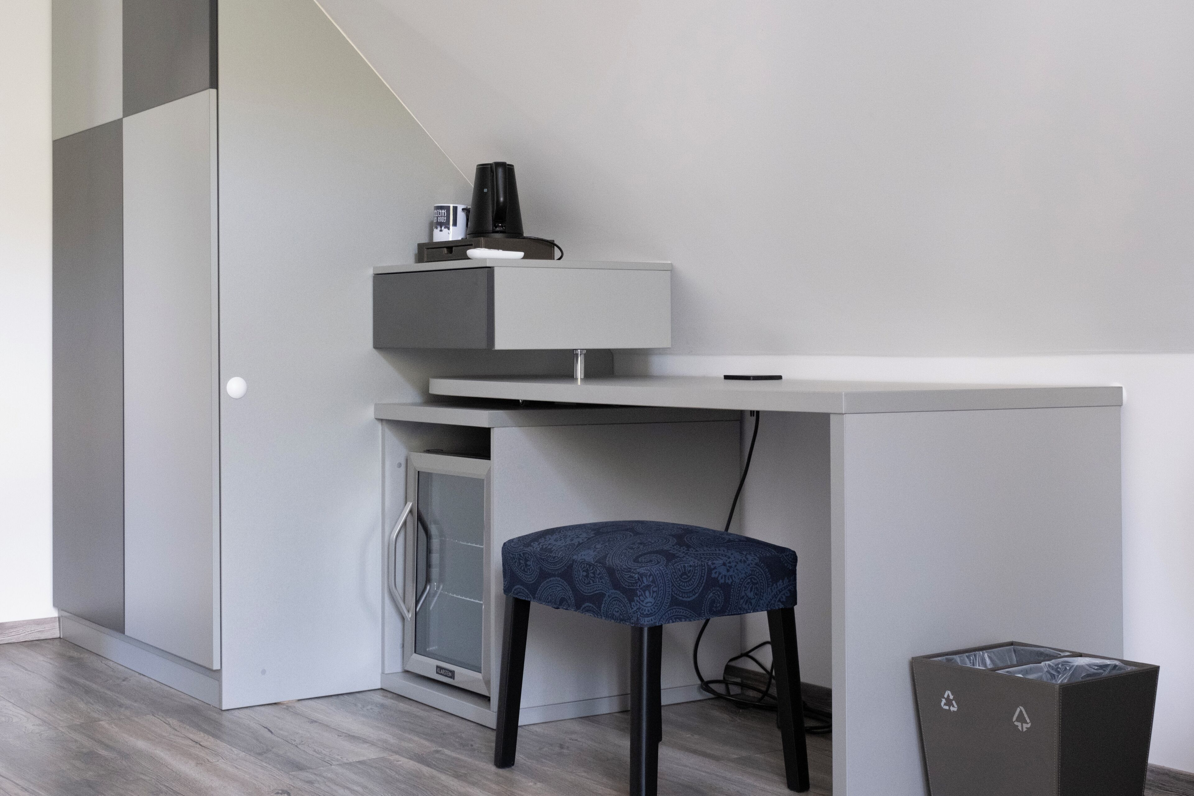 Habitació moderna i minimalista amb escriptori integrat, una cadira, un petit armari i un gresol.