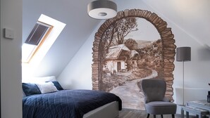 A bedroom with a bed, a chair, a table, a lamp, and a mural of a house.