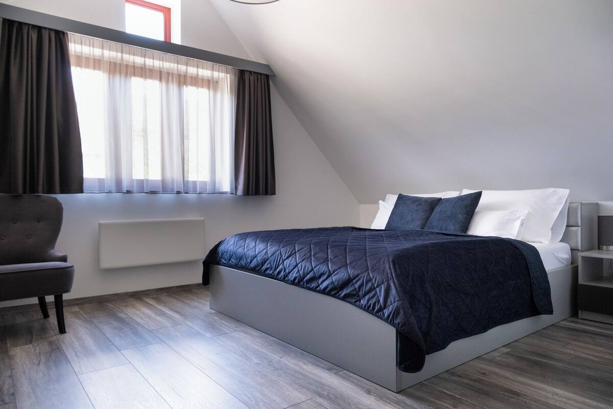 A modern bedroom with a bed, a chair, a nightstand, and a window with curtains.