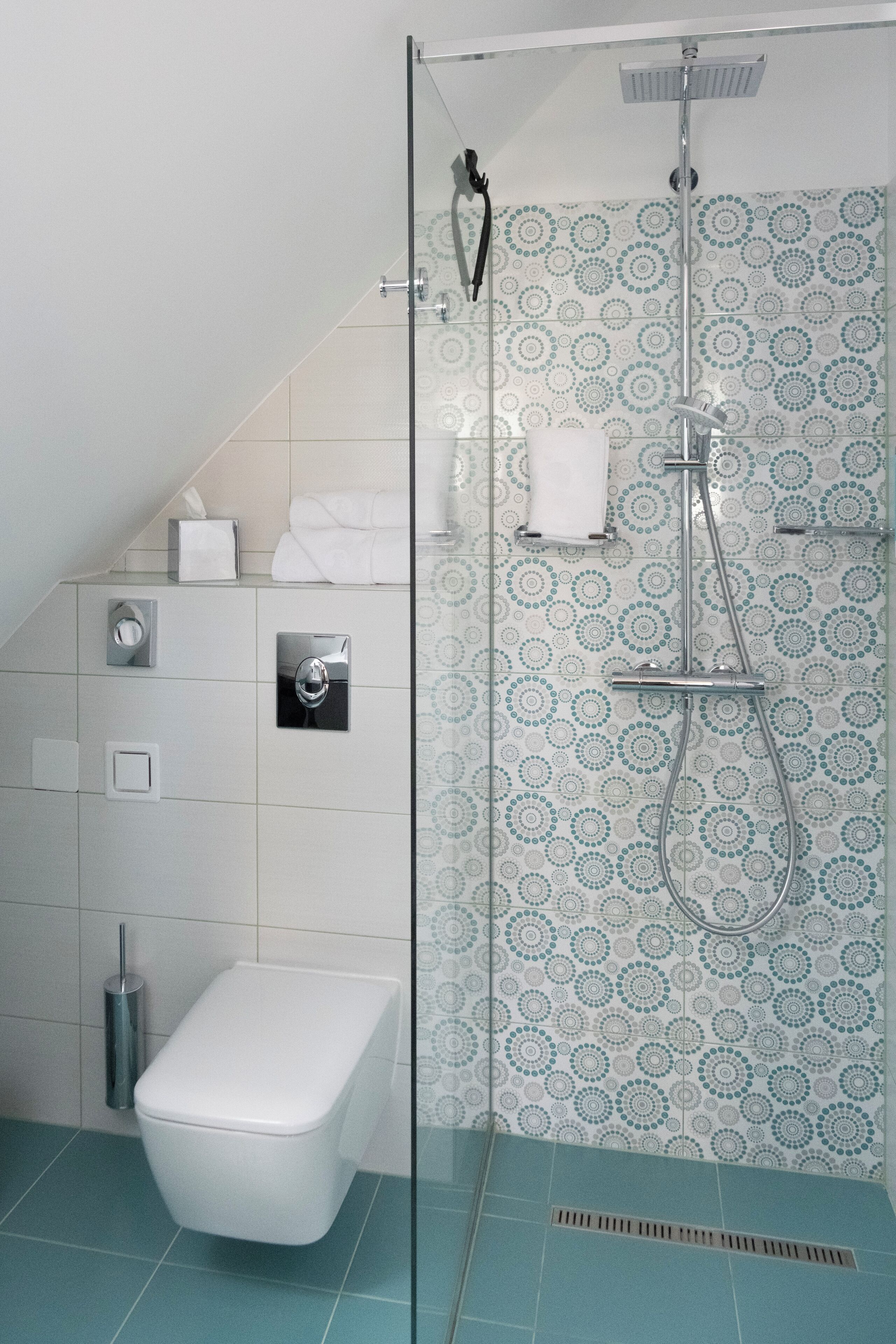 A modern bathroom with a glass-enclosed shower, a toilet, and a patterned tile wall.