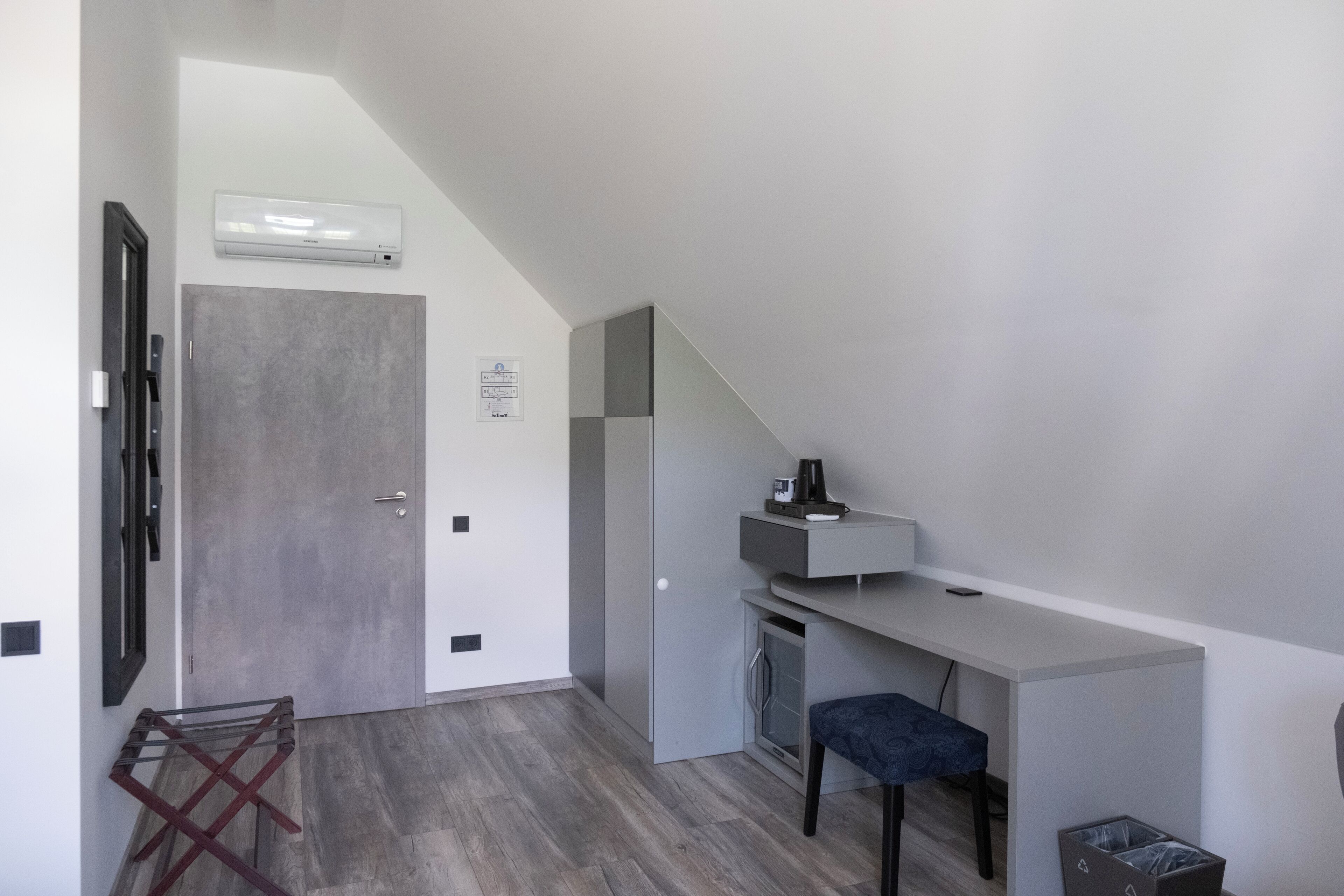 A modern, compact room with a built-in desk, a small seating area, and a door leading to another space.