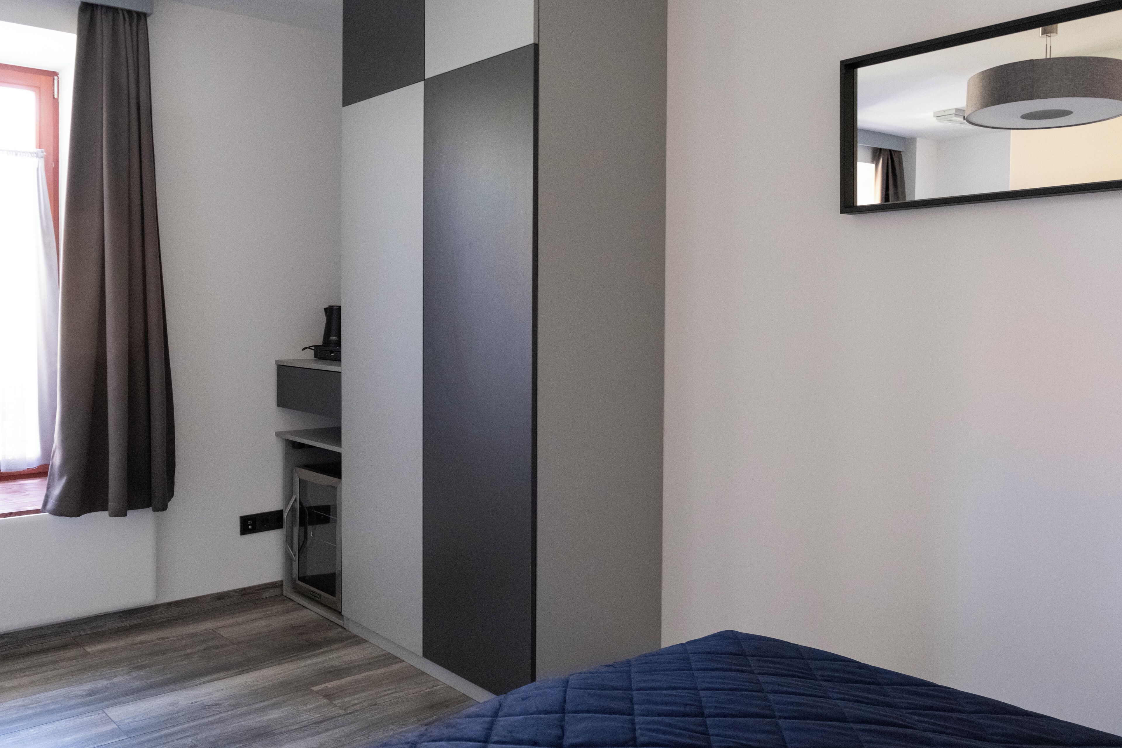 A bedroom with a bed, a wardrobe, a mirror, and a window with curtains.