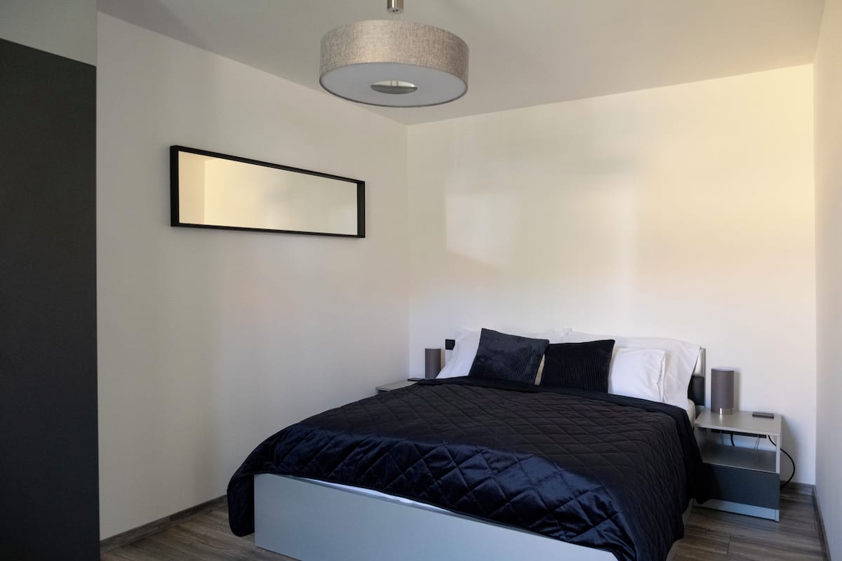 A modern bedroom with a bed, a bedside table, a lamp, and a wall-mounted mirror.