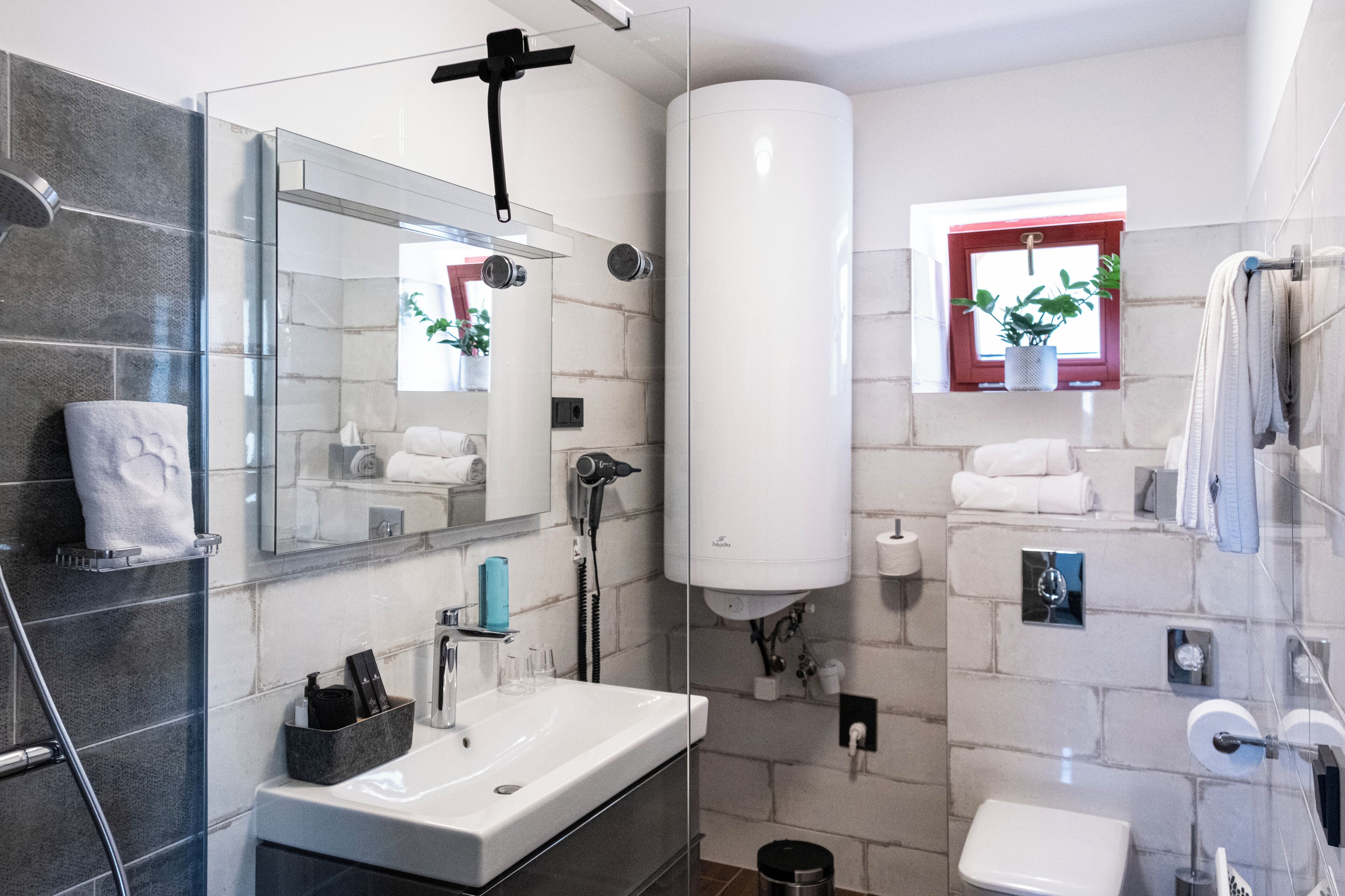 Un baño moderno con cabina de ducha de vidrio, un espejo grande, un lavamanos blanco y un perchero para toallas.