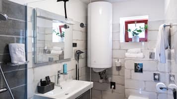 Un baño moderno con cabina de ducha de vidrio, un espejo grande, un lavamanos blanco y un perchero para toallas.