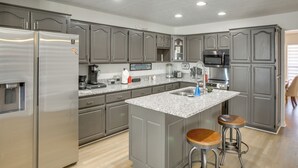 A modern kitchen with grey cabinets, stainless steel appliances, a granite countertop, and two bar stools. - Private Deck & Game Room: Portland Group Getaway (Portland)