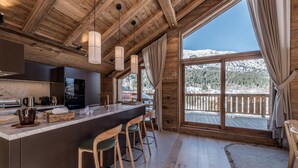 A wooden cabin interior with a kitchen, bar area, and large windows offering a mountain view. - Luxury penthouse with terrace, sauna, and hot tub, 5 bedrooms (Les Allues)