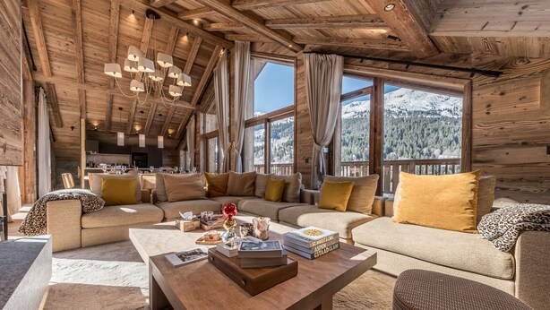 A cozy log cabin interior with a wooden ceiling, large windows offering mountain views, a plush sofa set, and a central coffee table. - Luxury penthouse with terrace, sauna, and hot tub, 5 bedrooms (Les Allues)