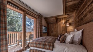 A bedroom with a large bed, wooden walls, a balcony with a chair, and a view of trees. - Luxury penthouse with terrace, sauna, and hot tub, 5 bedrooms (Les Allues)