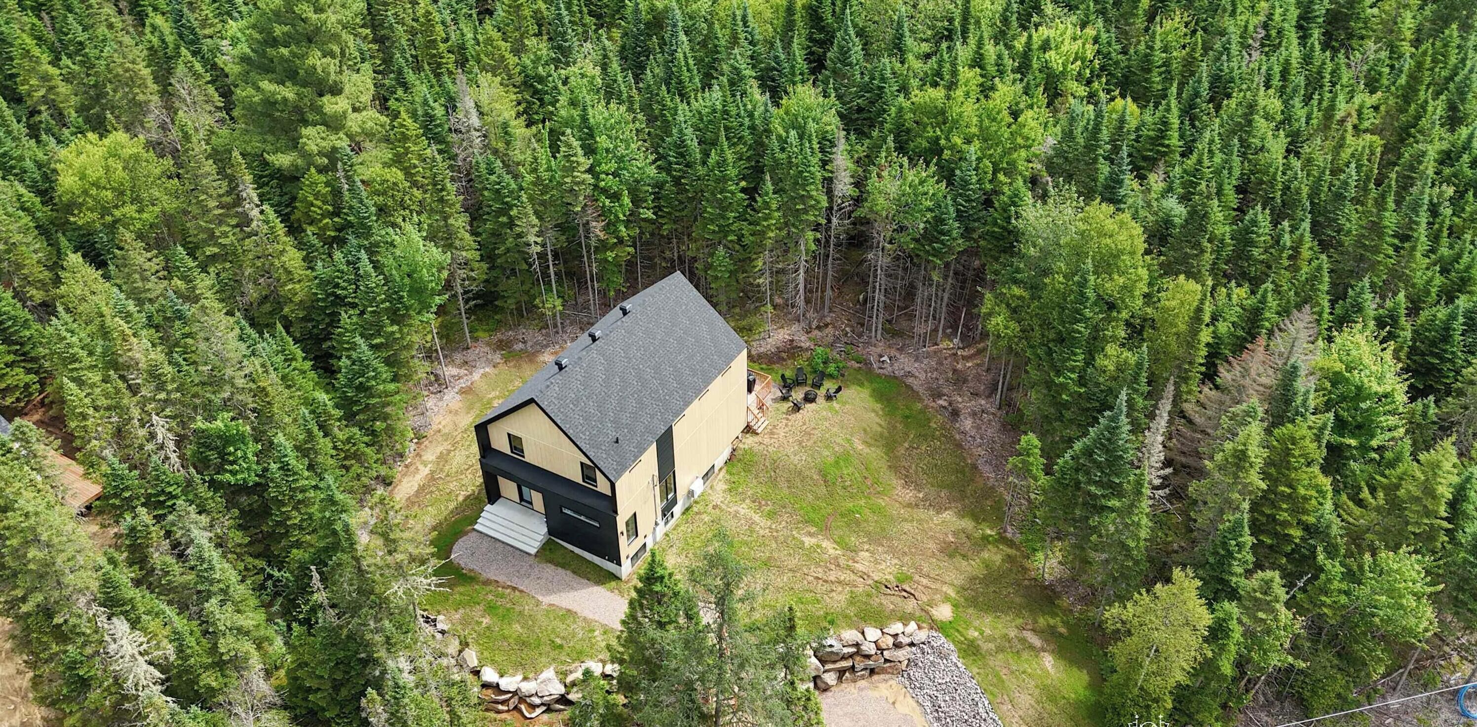 Une maison moderne à deux étages, entourée d’une forêt dense.
