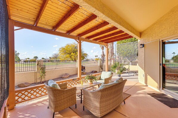 Ein überdachter Patio-Bereich mit Rattanmöbeln, einem kleinen Tisch und einem Blumentopf.