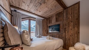 A bedroom with a wooden ceiling, a bed with white linens, a mounted TV, and a view of snow-capped mountains. - Luxury apartment, 3 bedrooms, fireplace, concierge 5*, ski room, non-smoking (Les Allues)