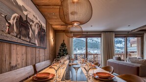 A dining area with a long wooden table set for a meal, a Christmas tree, and a view of mountains through large windows. - Luxury apartment, 3 bedrooms, fireplace, concierge 5*, ski room, non-smoking (Les Allues)