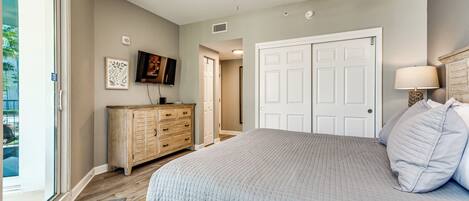A bedroom with a bed, a ceiling fan, a dresser, a television, and a door.