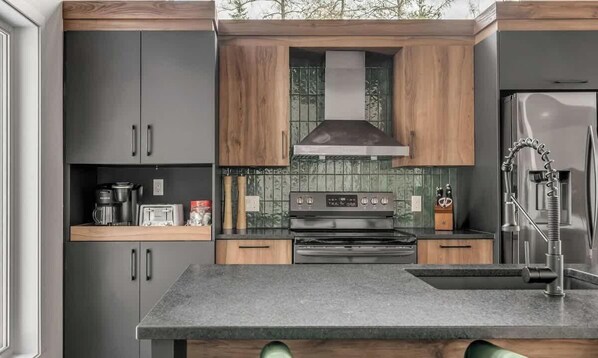 Een moderne keuken met donkere kastjes, een houten aanrechtblad, een roestvrijstalen fornuis en een inbouwoven.