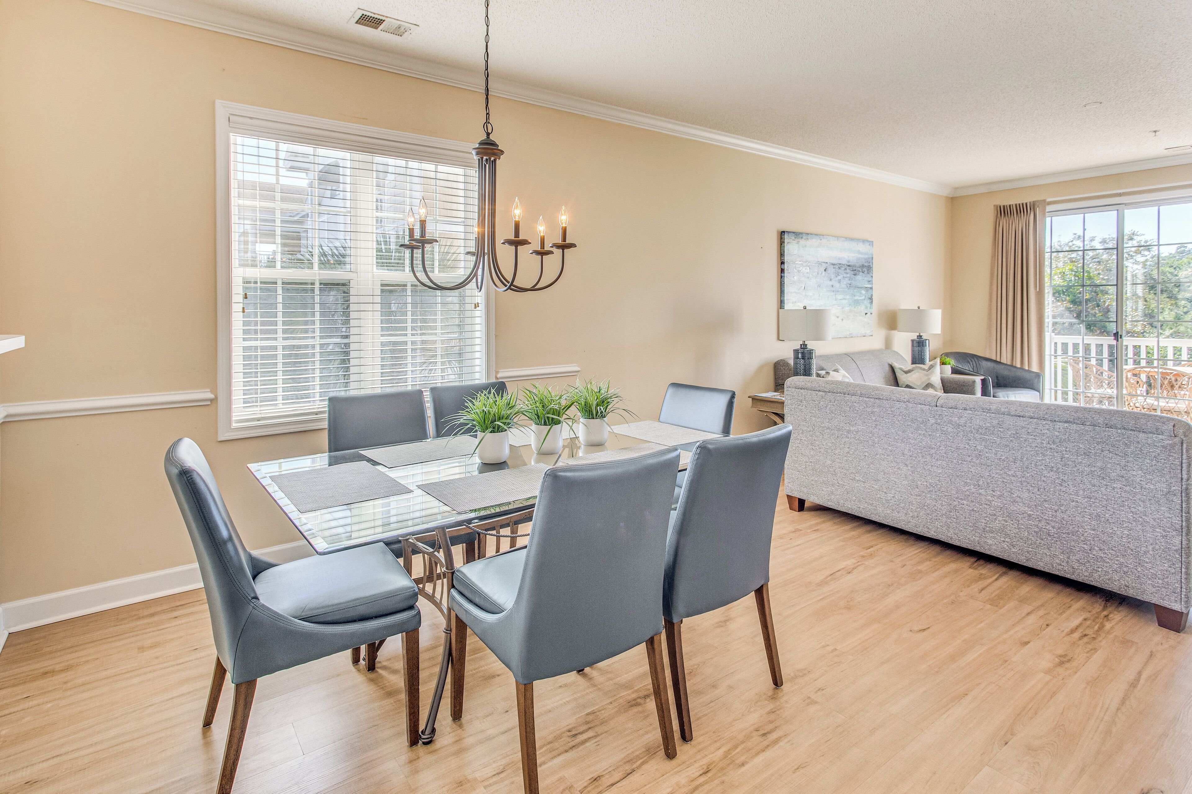 A dining area with a glass-top table, grey upholstered chairs, and a chandelier.