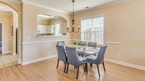 A dining area with a table and chairs, a chandelier, and a view of the kitchen. - Beach Shuttle & Pool: North Myrtle Beach Condo! (North Myrtle Beach)