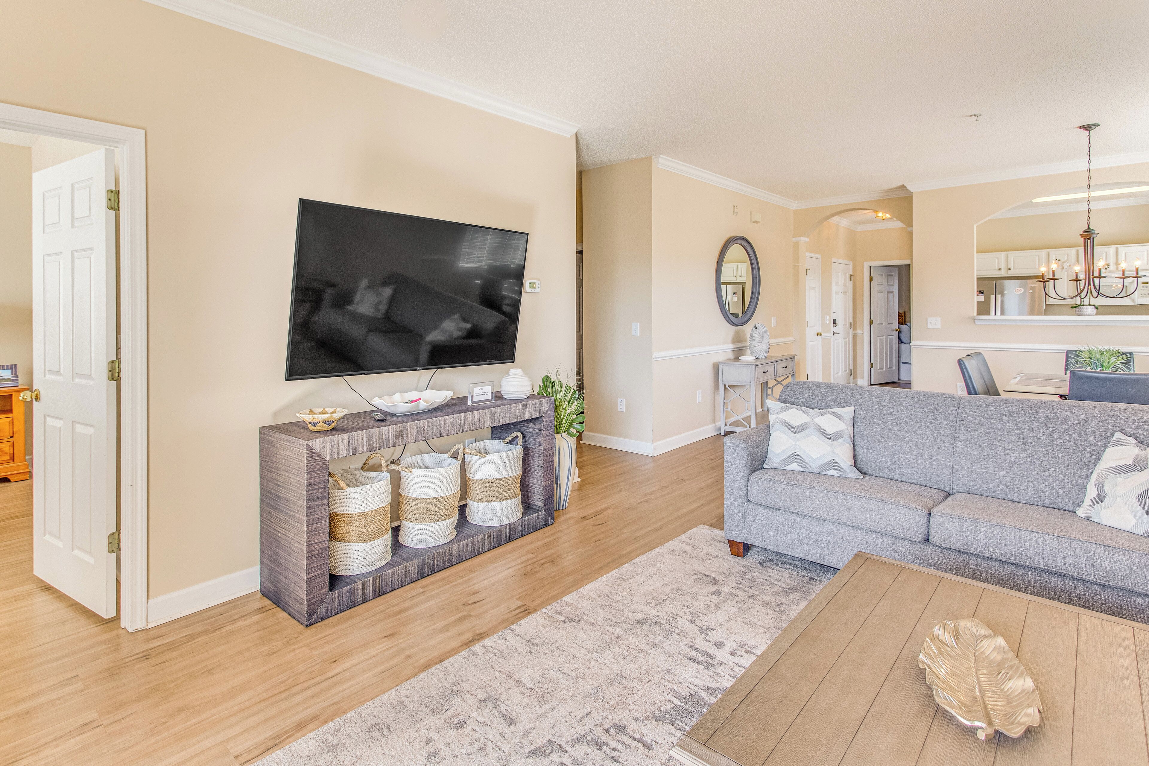 A living room with a television, grey sofa, wooden floor, and a coffee table.