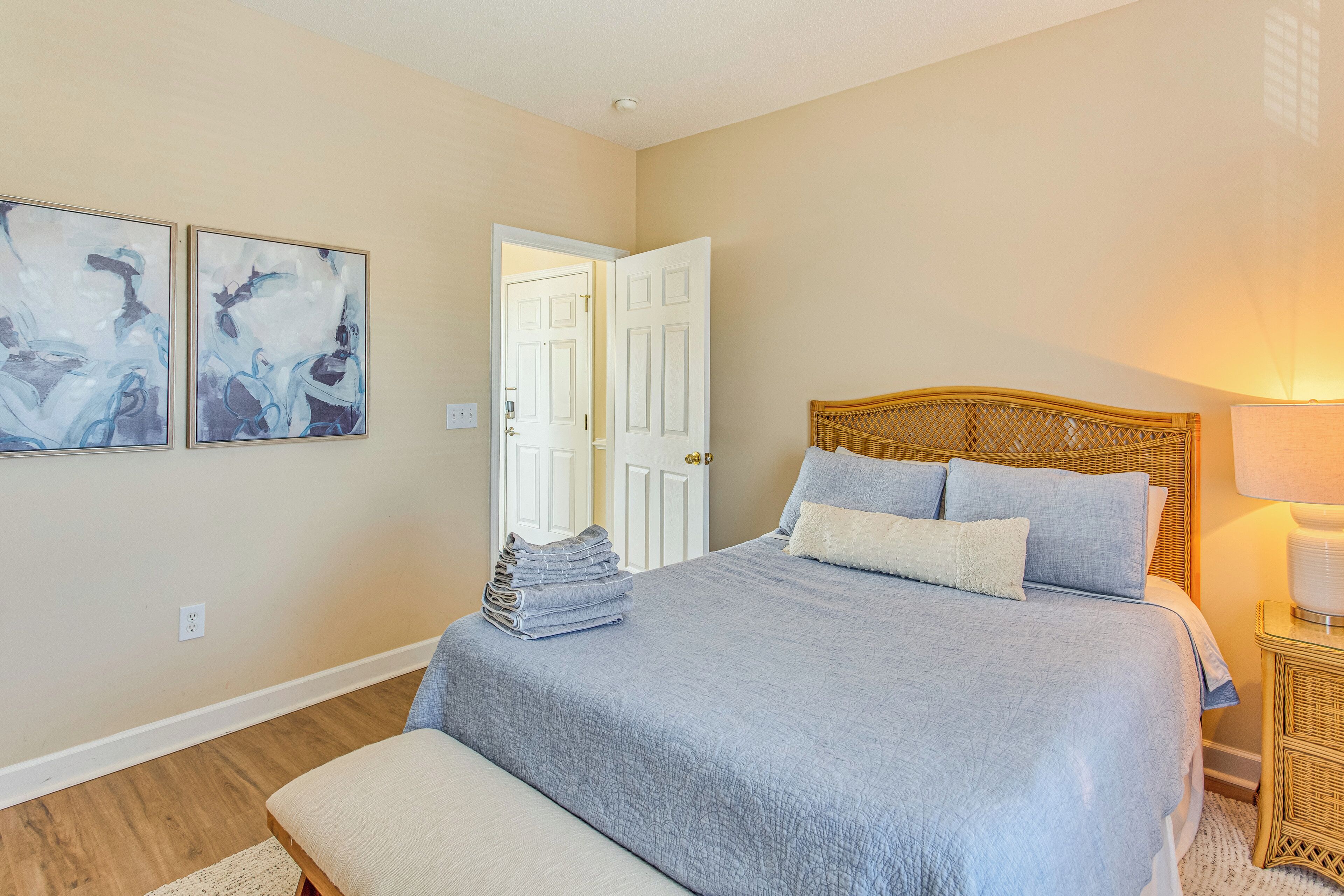 A bedroom with a bed, a bedside table, a lamp, and two wall-mounted paintings.