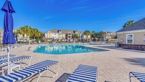 A pool area with lounge chairs and umbrellas, surrounded by buildings with a brick facade. - Beach Shuttle & Pool: North Myrtle Beach Condo! (North Myrtle Beach)
