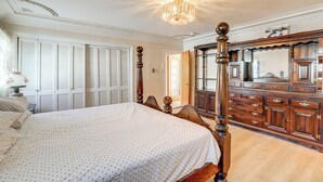 Quarto com cama grande, guarda-roupa de madeira e um candelabro.