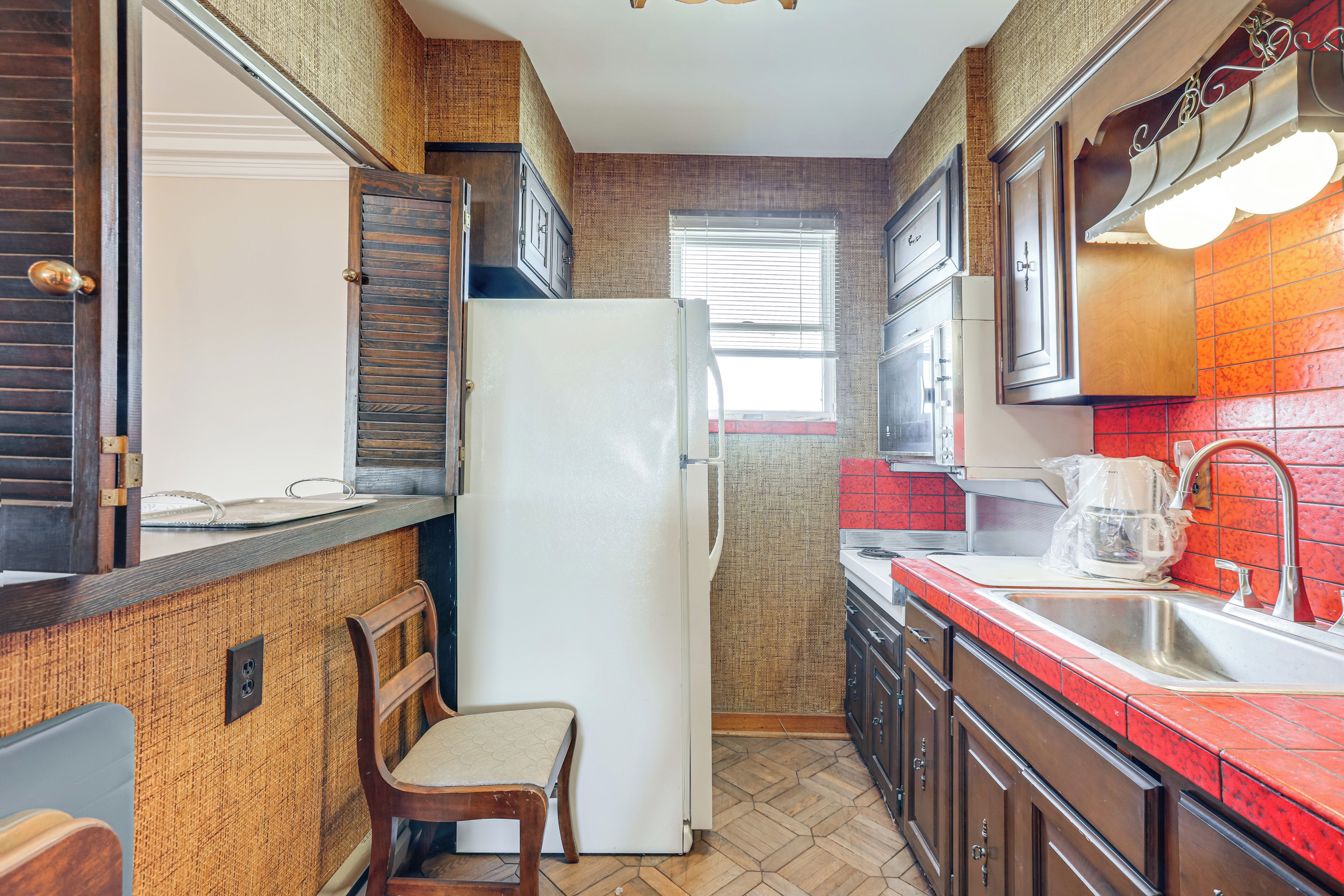 A kitchen with a refrigerator, wooden cabinets, a sink, and a chair.