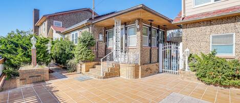 A residential house with a tiled patio, a gated entrance, and a small front yard with a lamp post and potted plants.