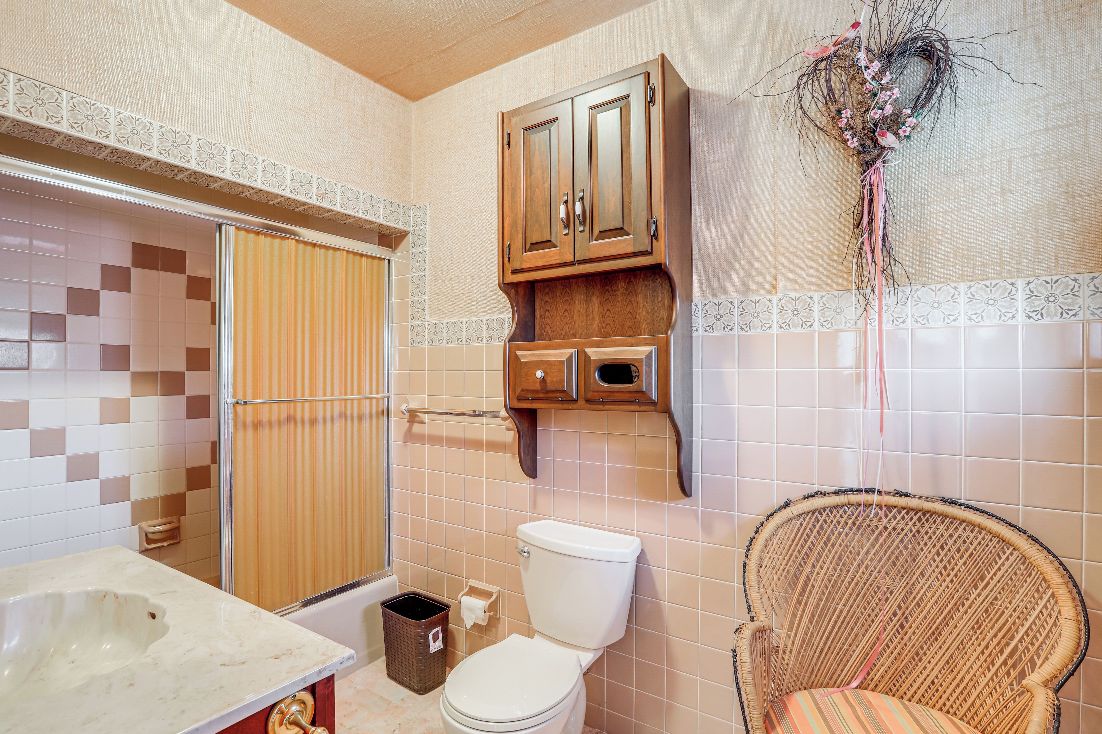 Ein Badezimmer mit Toilette, Waschbecken, Dusche und Korbsessel.