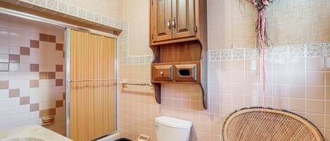 Ein Badezimmer mit Toilette, Waschbecken, Dusche und Korbsessel.