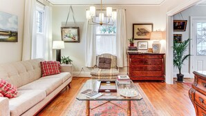 A cozy living room with a sofa, armchair, wooden dresser, and a glass coffee table. - 3 Mi to Augusta National: Historic Home w/ Patio (Augusta)