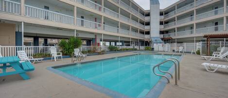 A multi-story hotel with a swimming pool, outdoor seating, and a covered area.