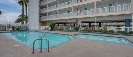 A multi-story hotel with a swimming pool, palm trees, and a white fence.