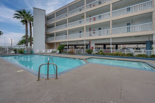 A multi-story hotel with a swimming pool, palm trees, and a white fence.