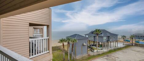 A beachfront property with a balcony overlooking the ocean, a covered patio, and a sandy beach area.